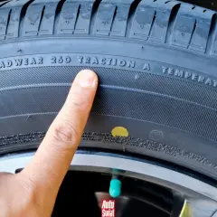 Palec wskazuje żółtą kropkę na oponie, obok napisu "TREADWEAR 260 TRACTION A TEMPERATURE A".