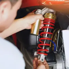 Mechanik dokonuje wymiany amortyzatorów tył w motocyklu, trzymając nowy element.