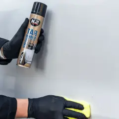 Ręce w czarnych rękawiczkach używają preparatu K2 Tar Remover, by pokazać, jak usunąć naklejki z samochodu.