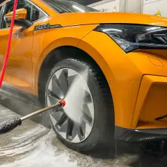 Pomarańczowe auto lśni po tym, jak dowiedzieliśmy się, jak myc auto. Woda pod ciśnieniem spływa po karoserii, usuwając brud.