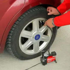 Osoba w czerwonej kurtce pompuje koło w samochodzie Ford. Auto sciaga na prawa strone, więc trzeba uzupełnić powietrze.