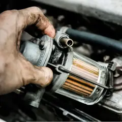 Brudne ręce mechanika sprawdzają filtr paliwa. Zapchany filtr gazu objawy mogą być różne, od spadku mocy po problemy z uruchomieniem silnika.