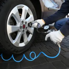 Osoba w rękawiczkach dokonuje pompowania opon samochodu za pomocą manometru.