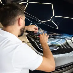 Mężczyzna aplikuje folię ochronną PPF na reflektor luksusowego samochodu. To świetny sposób na ochronę lakieru.
