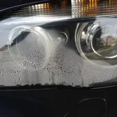 Zaparowane reflektory BMW z licznymi kropelkami wody wewnątrz.
