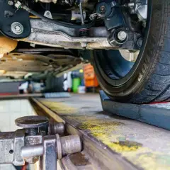 Podnośnik samochodowy pod kołem, mechanik sprawdza geometrię kół co to za proces.