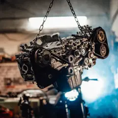Silnik zawieszony na łańcuchach, z widocznym skomplikowanym układem pasków i kół zębatych. Może to być moment, gdy mechanik diagnozuje objawy rozrządu.