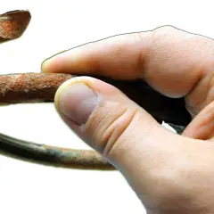 Dłoń trzyma zardzewiały, pęknięty element, który wygląda jak sprężyna w aucie po długiej eksploatacji.