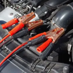 Kable rozruchowe podłączone do akumulatora, bo auto nie odpala. Miedziane klamry i czerwono-czarne uchwyty.