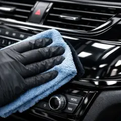 Ręka w czarnej rękawiczce poleruje błyszczące piano black w samochodzie, przywracając mu głębię koloru.