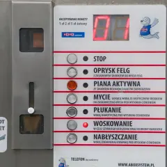 Panel myjni samochodowej z przyciskami: STOP, OPRYSK FELG, PIANA AKTYWNA, MYCIE, PŁUKANIE, WOSKOWANIE, NABŁYSZCZANIE. Instrukcja jak myć samochód na myjni.