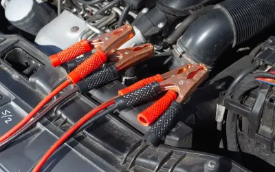 Kable rozruchowe podłączone do akumulatora, bo auto nie odpala. Miedziane klamry i czerwono-czarne uchwyty.