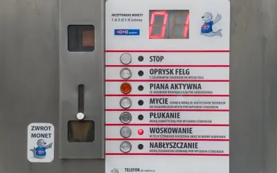 Panel myjni samochodowej z przyciskami: STOP, OPRYSK FELG, PIANA AKTYWNA, MYCIE, PŁUKANIE, WOSKOWANIE, NABŁYSZCZANIE. Instrukcja jak myć samochód na myjni.