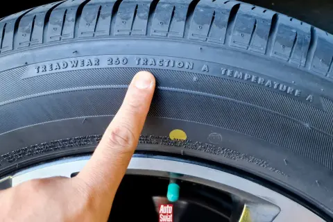 Palec wskazuje żółtą kropkę na oponie, obok napisu "TREADWEAR 260 TRACTION A TEMPERATURE A".