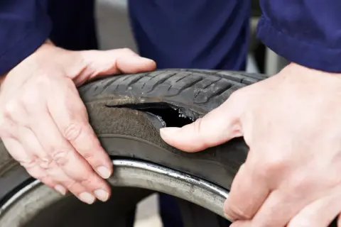 Dłonie mechanika badają oponę po głośnym wystrzale. Widoczne jest duże rozdarcie bieżnika.