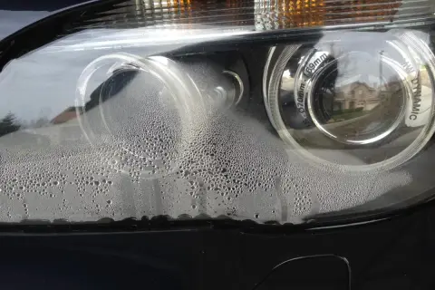 Zaparowane reflektory BMW z licznymi kropelkami wody wewnątrz.