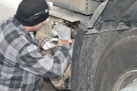 Mechanik w rękawiczkach pracuje przy samochodzie ciężarowym, próbując dowiedzieć się, jak wyczyścić dpf domowym sposobem.