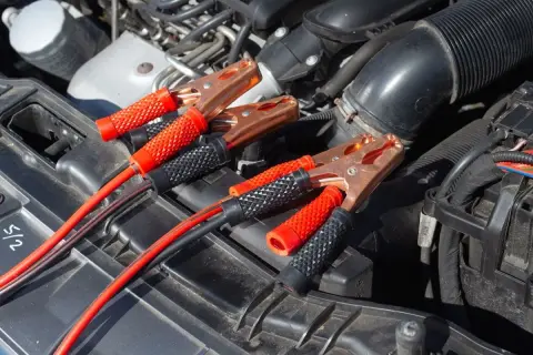 Kable rozruchowe podłączone do akumulatora, bo auto nie odpala. Miedziane klamry i czerwono-czarne uchwyty.