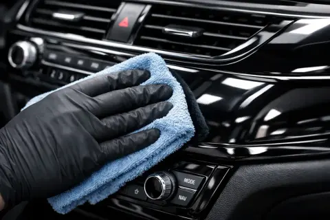 Ręka w czarnej rękawiczce poleruje błyszczące piano black w samochodzie, przywracając mu głębię koloru.