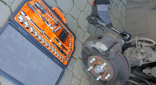 Ręka w rękawicy odkręca zapieczoną śrubę przy hamulcu. Obok walizka z narzędziami.
