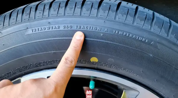 Palec wskazuje żółtą kropkę na oponie, obok napisu "TREADWEAR 260 TRACTION A TEMPERATURE A".
