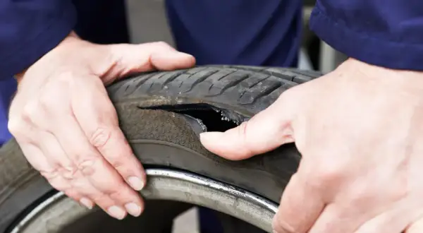 Dłonie mechanika badają oponę po głośnym wystrzale. Widoczne jest duże rozdarcie bieżnika.