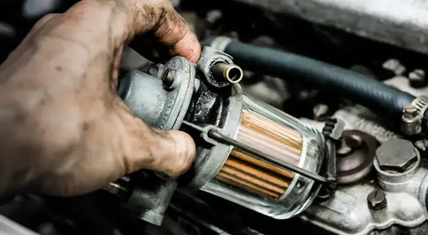 Brudne ręce mechanika sprawdzają filtr paliwa. Zapchany filtr gazu objawy mogą być różne, od spadku mocy po problemy z uruchomieniem silnika.