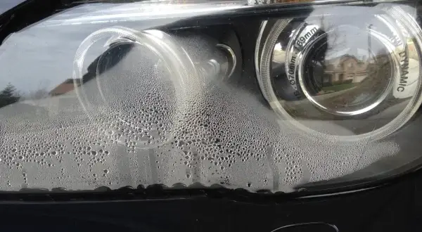 Zaparowane reflektory BMW z licznymi kropelkami wody wewnątrz.