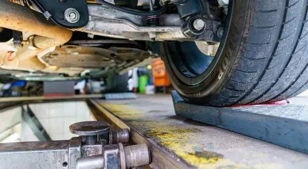 Podnośnik samochodowy pod kołem, mechanik sprawdza geometrię kół co to za proces.