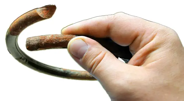 Dłoń trzyma zardzewiały, pęknięty element, który wygląda jak sprężyna w aucie po długiej eksploatacji.