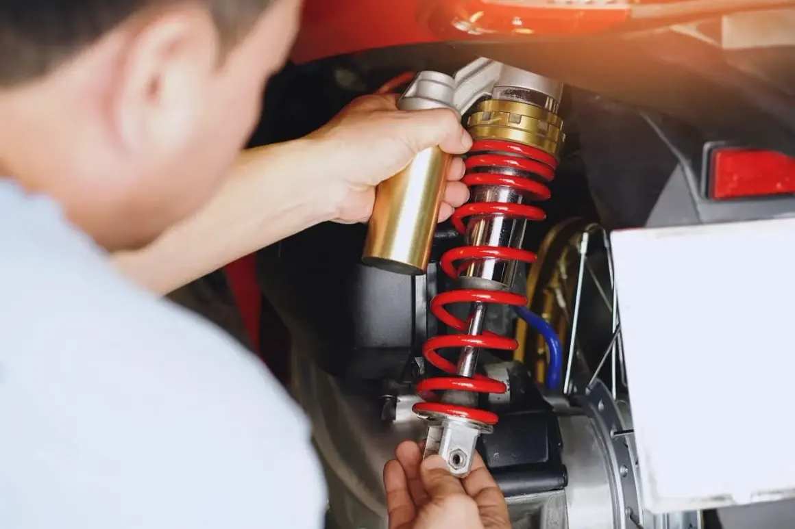 Mechanik dokonuje wymiany amortyzatorów tył w motocyklu, trzymając nowy element.