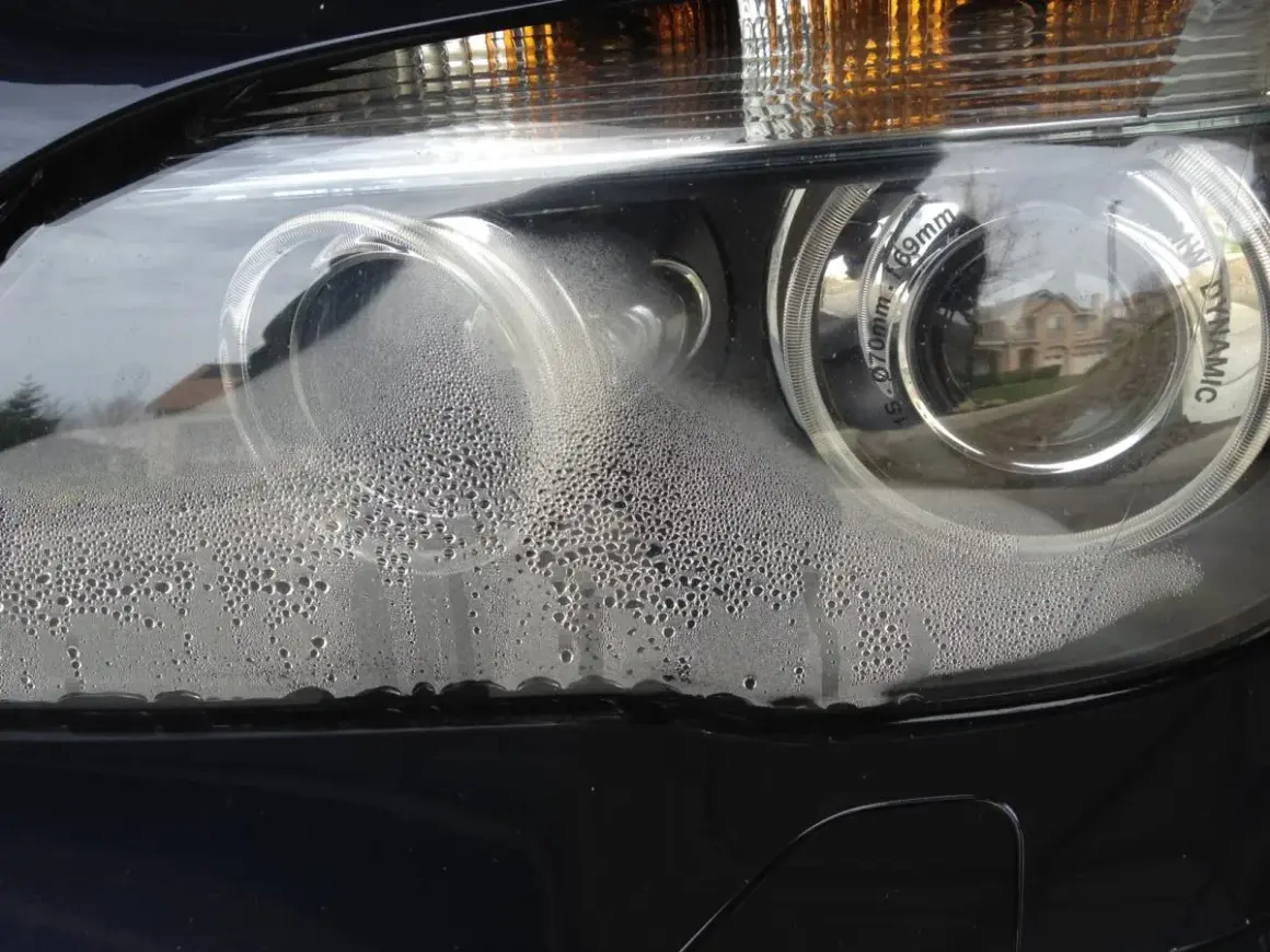 Zaparowane reflektory BMW z licznymi kropelkami wody wewnątrz.