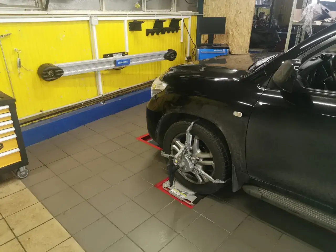 Czarny SUV na podnośniku z zamontowanymi czujnikami do pomiaru prawidłowej zbieżności k&oacute;ł.