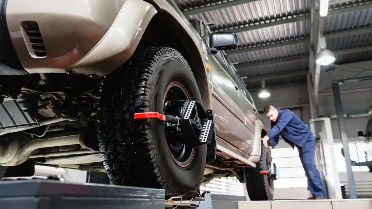 Mechanik sprawdza geometrię k&oacute;ł SUV-a. Urządzenie na kole pomaga ustawić kąty nachylenia.