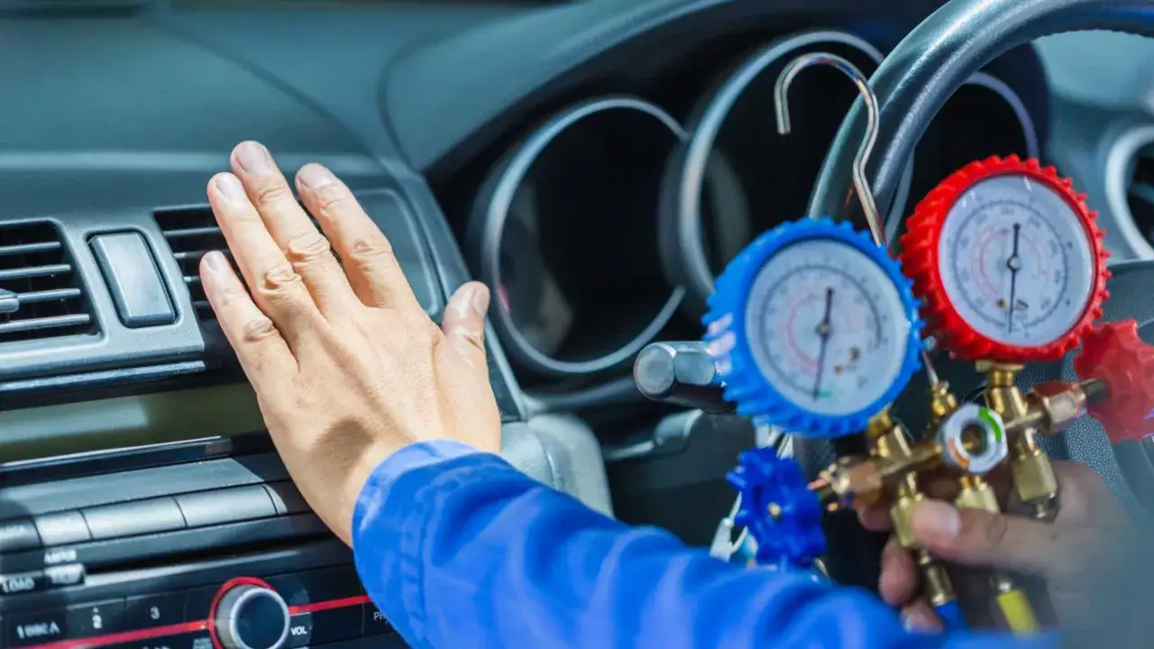 Mechanik sprawdza ciśnienie w układzie klimatyzacji samochodowej, przygotowując uzupełnienie czynnika chłodzącego.