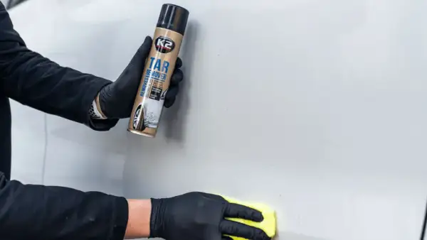 Ręce w czarnych rękawiczkach używają preparatu K2 Tar Remover, by pokazać, jak usunąć naklejki z samochodu.