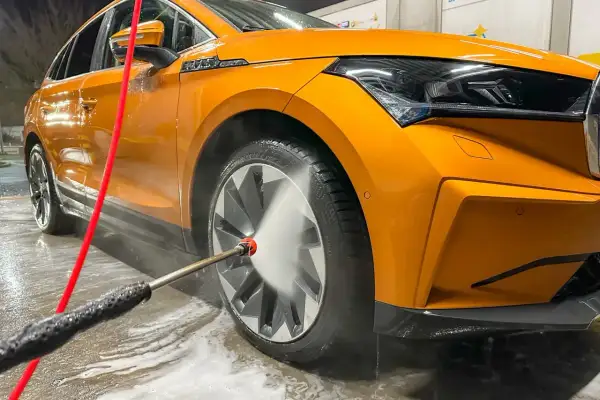 Pomarańczowe auto lśni po tym, jak dowiedzieliśmy się, jak myc auto. Woda pod ciśnieniem spływa po karoserii, usuwając brud.