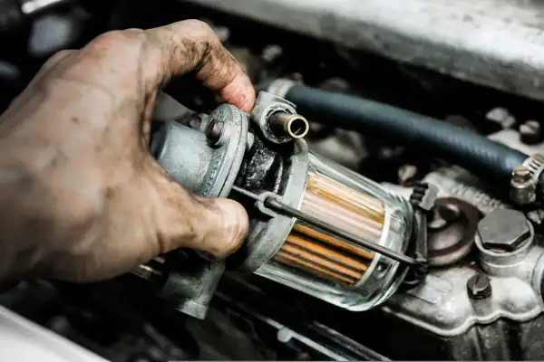 Brudne ręce mechanika sprawdzają filtr paliwa. Zapchany filtr gazu objawy mogą być różne, od spadku mocy po problemy z uruchomieniem silnika.