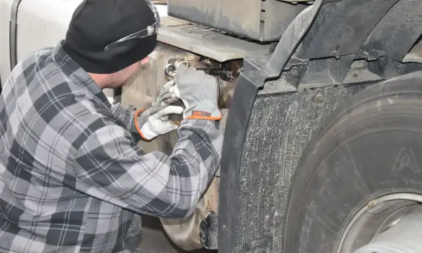 Mechanik w rękawiczkach pracuje przy samochodzie ciężarowym, próbując dowiedzieć się, jak wyczyścić dpf domowym sposobem.