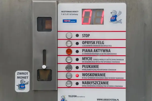 Panel myjni samochodowej z przyciskami: STOP, OPRYSK FELG, PIANA AKTYWNA, MYCIE, PŁUKANIE, WOSKOWANIE, NABŁYSZCZANIE. Instrukcja jak myć samochód na myjni.